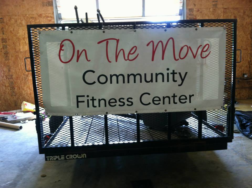 A sign tied to the back of a trailer advertising a community fitness center.