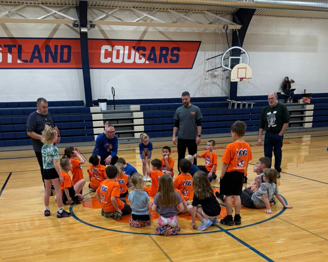 Young kids gathered in a gym wearing uniforms with several adults around them.
