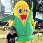 Someone dressed in a corn mascot costume poses with a child.