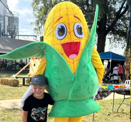 Someone dressed in a corn mascot costume poses with a child.