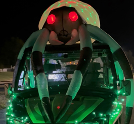 A giant inflatable spider lit up with lights on top of a vehicle.